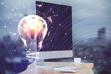 Computer on desktop in office with bulb icon hologram. Multi exposure. Concept of idea.