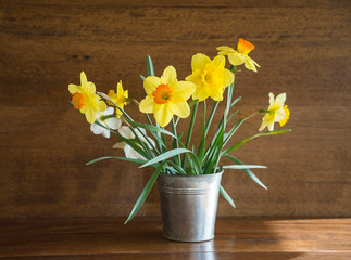 Easter and spring holiday concept. Bouquet of yellow daffodils in metallic vase on the vintage wood background