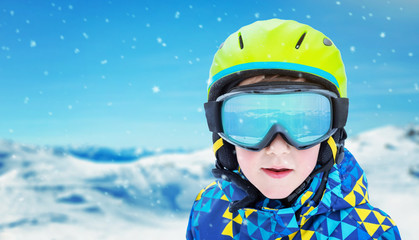 Boy with modern ski green helmet, yellow glasses and blue jacket. Reflection of snowy peaks on...