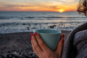 Young woman enjoying cup of english breakfast tea, enjoying evening by the sea in winter time.