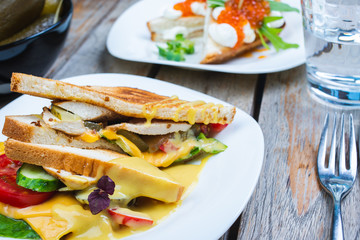 Classic breakfast, hot sandwiches with cheese, vegetables and chicken on a wooden table. Hand-made, rustic breakfast, toast with turkey and vegetables. Soft focus.