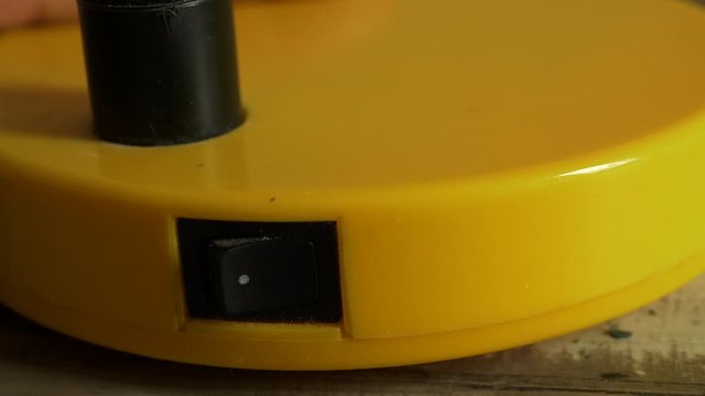 close-up of an elderly person’s finger turns on the power button of yellow LED lamp to illuminate computer keyboard. Blurred on / off button concept as background. 4K