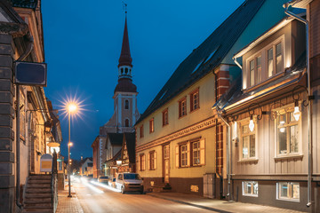 Fototapeta na wymiar Parnu, Estonia. Night Puhavaimu Street With Old Wooden Houses, Restaurants, Cafe, Hotels And Shops In Evening Night Illuminations. View Of Lutheran Church Of St. Elizabeth