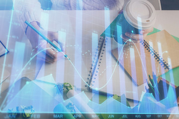 Financial forex graph displayed on hands taking notes background. Concept of research. Multi exposure