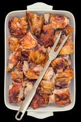 Freshly Spit Roasted Pork Thigh Meat Slices in White Ceramic Casserole Pan with Serving Fork Isolated on Black Background