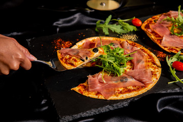 Pizza Jamon Ibérico and Rocket salad served on slate table, black background, Close up