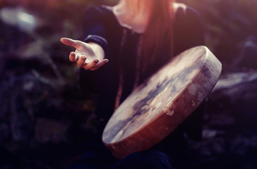 beautiful shamanic girl playing on shaman frame drum in the nature.