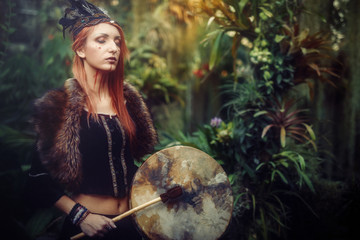beautiful shamanic girl playing on shaman frame drum in the nature.