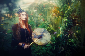 Naklejka premium beautiful shamanic girl playing on shaman frame drum in the nature.