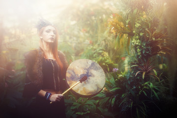 beautiful shamanic girl playing on shaman frame drum in the nature.