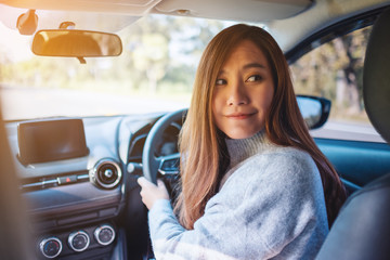 Closeup image of a woman holding steering wheel and looking back while driving in reverse on the road