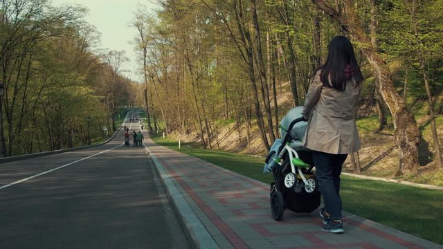 Young mother walking with baby carriage at park. Casual woman having sidewalk