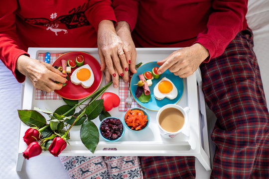 Hands of an elderly couple enjoying their breakfast at the bed. St Valentine’s concept.