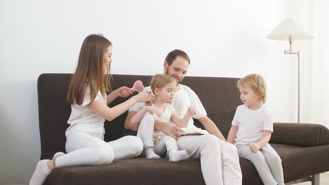 Happy friendly family consisted of mother father and children enjoy spending time together at home, sitting on sofa and wearing white casual clothes