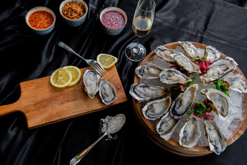 Fresh Oysters with lemon and white wine in wooden bucket and plate, top view, dark background 