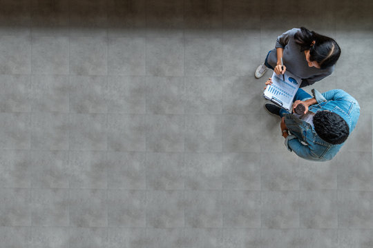 Top View Of Young Asian Business Team Standing, Talking And Reporting With Annual Report Document In Modern Workplace. Above View Of Casual Creative Team Discussion With Report Performance.