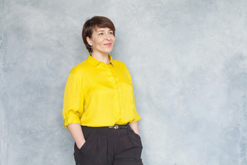 Pretty middle aged business woman in yellow shirt on gray background