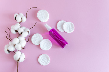 Facial tonic or makeup remover and cotton pads for face care on pink background top view, flat lay.