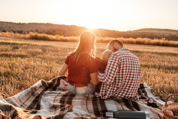 Happy Young Family Mom and Dad with Their Little Son Enjoying Summer Weekend Picnic Outside the City in the Field at Sunny Day Sunset, Vacation Time Concept