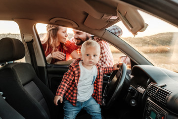 Happy Young Family Mom and Dad with Their Son Little Driver Enjoying Summer Weekend Picnic on the Car Outside the City in the Field at Sunny Day Sunset, Vacation and Road Trip Concept