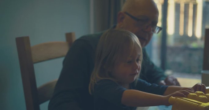 Toddler and grandfather playing with toy car at dining table