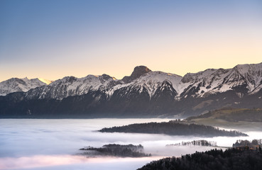 Plakat swiss mountain range in switzerland while the valley is covered in fog during sunset, super warm light and clear sky