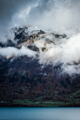 cloudy waterfront of a blue lake in switzerland while the mountains are covered in snow