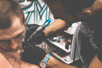 Tattoo salon. The tattoo master is tattooing a man on his shoulder. Tattoo machine, safety and...
