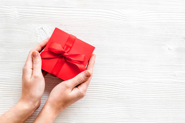 Give a gift on Valentine's Day. Women hand hold beautiful red present box on white wooden background top-down copy space