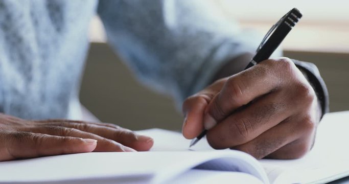 African left-handed businessman holding pen writing in organizer, close up