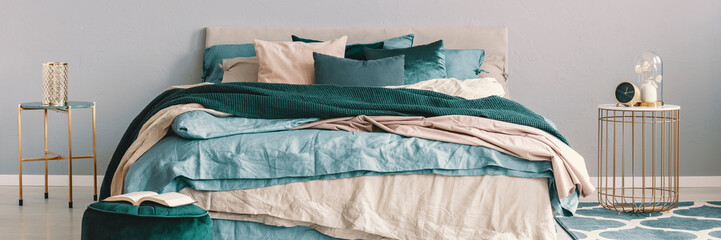 King size bed with beige, blue and emerald green bedding between two stylish nightstands in...