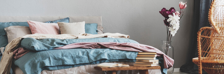 Pile of books on wooden bench in elegant bedroom interior with pastel pink, beige and blue bedding