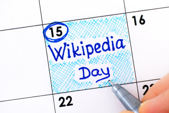 Woman fingers with pen writing reminder Wikipedia Day in calendar.