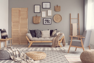 Stylish vintage armchair in contemporary living room interior with futon settee and wooden scandinavian ladder with blanket