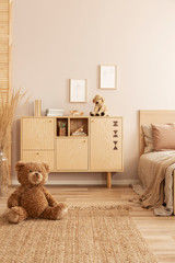 Cute brown teddy bear sitting on the floor of beige bedroom interior with wooden commode