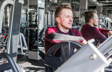 Young attractive adult man in a fitness gym. Sport training indoors. He is standing by the window...