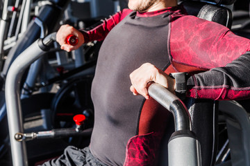 Training apparatus gym for man pumping muscles sitting on bench. Chest Exercise with weight. He takes his hands in front of his chest in fitness center.