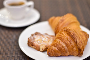 Croissant bread in a white plate on a wooden table with coffee.