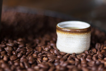A Small Cup of Hot Tea is Laid on a Pile of Brown Coffee Beans