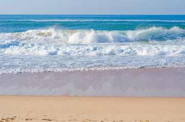 Picturesque beach in Portugal, ocean waves run ashore. Good weather for surfing.