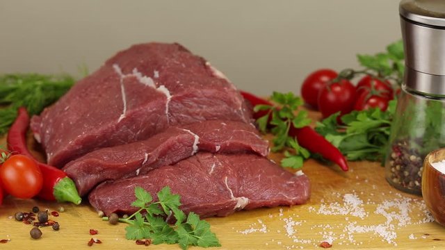 Beef steaks and vegetables on a wooden board on a gray background, close-up