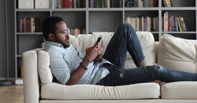 Young african guy using phone relax on sofa at home