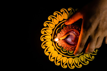 beautiful terracotta lamp placed with a hand on yellow rangoli and black background. diwali and insurance concept