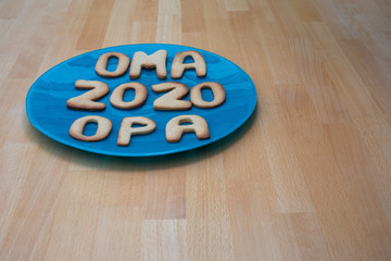 Kekse auf blaumenm Teller auf einem Holztisch mit den deutschen Wörtern  für Oma und Opa und der Jahreszahl 2020