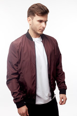Young european man in white sweater and black pants, red bomber jacket posing on white background. Isolated.