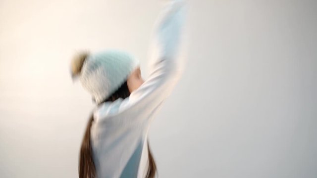 cool girl teenager in stylish white sweater and hat with pompom dances and laughs on light background closeup