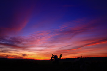 Fototapeta na wymiar Incredible very colorful sunset in the countryside. Silhouette of an industrial agricultural machine against the day. Cumulonimbus and stratus in a beautiful sky at night.