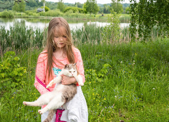 A young girl plays with a kitten on the grass in summer