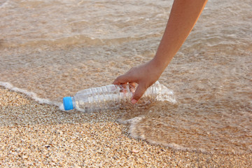 woman's hand collects plastic bottle on beach background. cleaning up beach. picking up plastic water bottle from the sandy beach. 