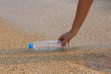 woman's hand collects plastic bottle on beach background. cleaning up beach. picking up plastic water bottle from the sandy beach. 